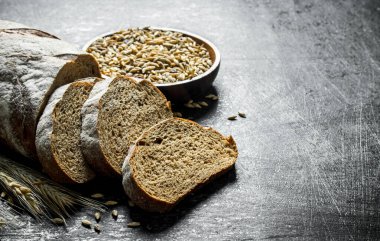 Dilimlenmiş çavdar ekmeği ve kasede tahıllar. Siyah rustik arka plan üzerinde