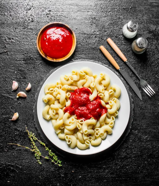 stock image Pasta and tomato sauce in bowl with thyme,garlic and spices. On black rustic background