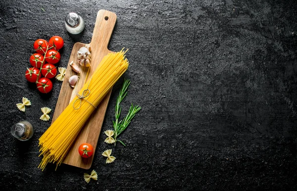 ニンニク トマト ローズマリーの木製のまな板の生スパゲッティ 黒い素朴な背景に — ストック写真