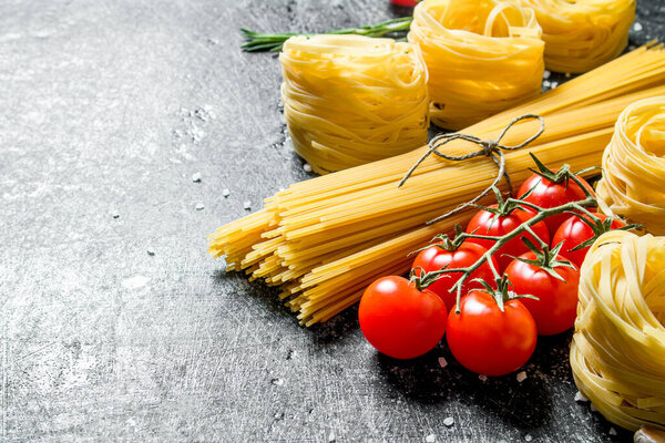 Spaghetti and tagliatelle raw with tomatoes. On black rustic background
