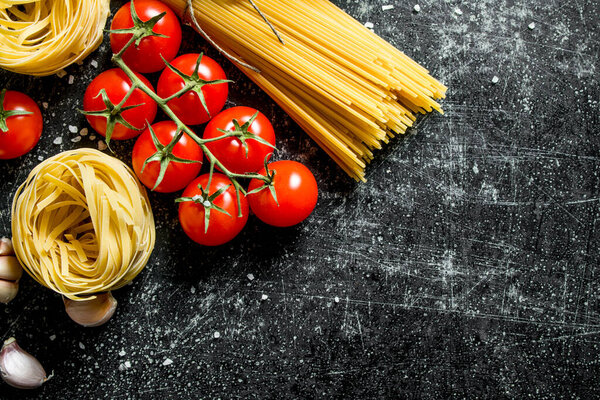 Spaghetti and tagliatelle raw with tomatoes. On black rustic background
