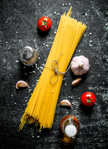 stock image Raw spaghetti with garlic cloves and tomato. On rustic background