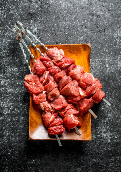 stock image Skewers with raw kebab on a wooden plate. On black rustic background