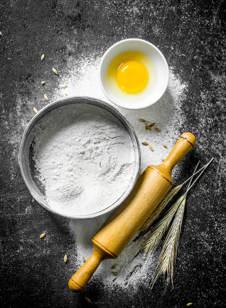 stock image Flour in a sieve with a rolling pin and spikelets. On dark rustic background