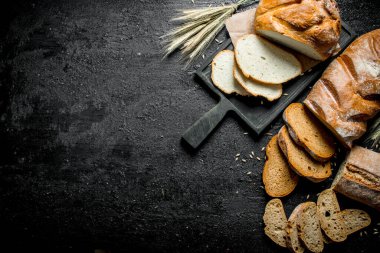 Farklı ekmek türlerinin parçaları. Siyah rustik arka plan üzerinde