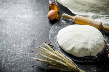 Fresh dough with spikelets and a rolling pin. On dark rustic background clipart