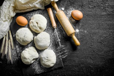 Yumurta ve oklava ile hamur yuvarlak parçalar. Siyah rustik arka plan üzerinde