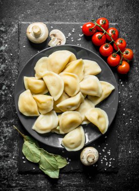 Dumplings on a plate and cherry tomatoes. On dark rustic background clipart