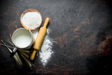 Bir sürahi içinde sivri, oklava ve süt ile un. Koyu rustik arka plan üzerinde