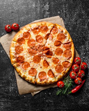 Domates ve biberiye ile kağıt üzerinde Pepperoni pizza. Koyu rustik arka plan üzerinde