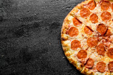 Salamlı dilimlenmiş biberli pizza. Siyah rustik arka plan üzerinde