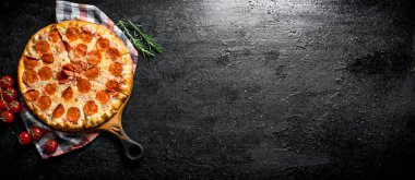 Peçetede salam lı ve peynirli pepperoni pizzası. Siyah rustik arka plan üzerinde