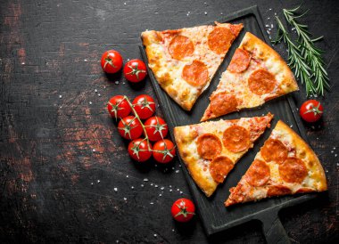 Domates ve biberiye ile pepperoni pizza dilimleri. Koyu rustik arka plan üzerinde