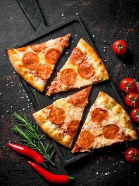 Biber, biberiye ve kiraz domates ile pepperoni pizza dilimleri. Koyu rustik arka plan üzerinde