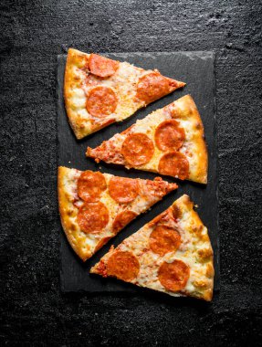 Sosis ve peynir ile pepperoni pizza dilimleri. Siyah rustik arka plan üzerinde