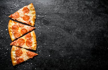 Dilimlenmiş biberpeynirli pizza ve salam. Siyah rustik arka plan üzerinde