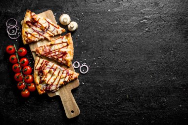 Bir dalda domates li dilimlenmiş barbekü pizzası. Siyah rustik arka plan üzerinde