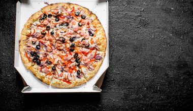 Kutuda deniz ürünleri olan pizza. Siyah rustik arka plan üzerinde