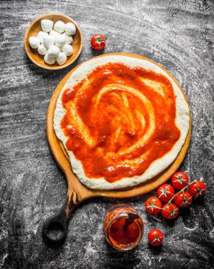 Çiğ pizza. Domates salçası, mozzarella ve taze domates ile hamur dışarı haddelenmiş. Rustik arka planda