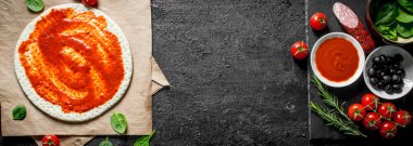 Hazır pizza. Domates salçası ile hamur dışarı haddelenmiş. Siyah rustik arka plan üzerinde