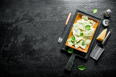 Ravioli paremesan, baharat ve ıspanak ile. Siyah rustik arka plan üzerinde