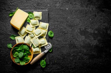 Ravioli parmesan ve ıspanak yaprakları ile çiğ. Siyah rustik arka plan üzerinde