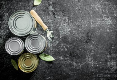 Konserve açacağı ve Bay yaprağı ile çeşitli konserve çeşitleri. Koyu rustik arka plan üzerinde