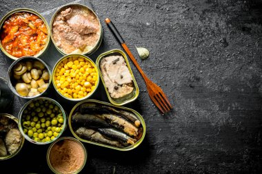 Açık kantlarda konserve yiyecekler. Siyah rustik arka plan üzerinde