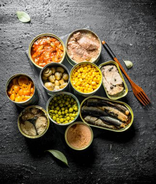 Konserve gıda ile farklı açık konserve konserve seti. Siyah rustik arka plan üzerinde