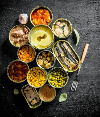 Çeşitli konserve gıda ile açık konserve konserveler. Siyah rustik arka plan üzerinde