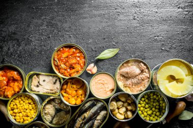 Açık kantlar içinde çeşitli konserve gıda. Siyah rustik arka plan üzerinde