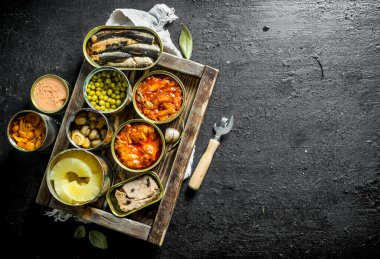 Tepside konserve çeşitli açık konserve konserve ler. Siyah rustik arka plan üzerinde