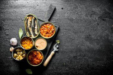 Kesme Tahtası'nda konserve konserve konserveleri açın. Siyah rustik arka plan üzerinde