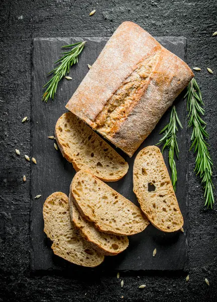 Biberiyeli taş bir tahtada dilimlenmiş ciabatta ekmeği. Siyah rustik arka plan üzerinde