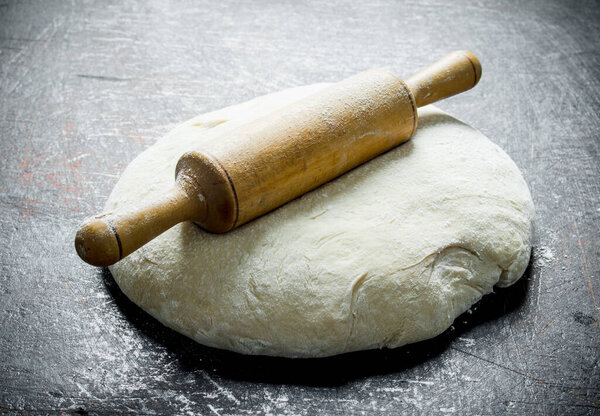 Freshly prepared dough with a rolling pin. On dark rustic background