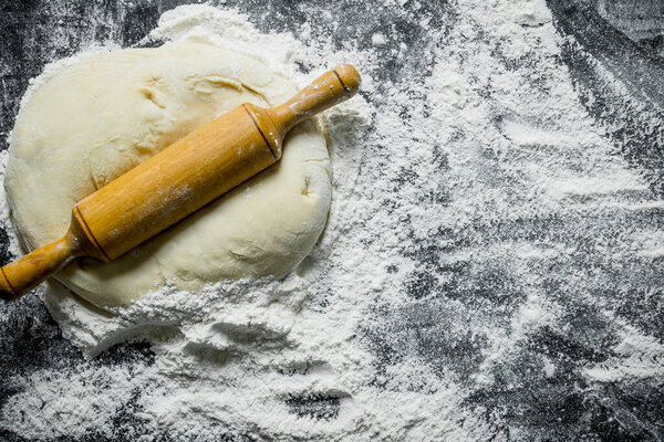 Flour background. The dough with a rolling pin. On rustic background