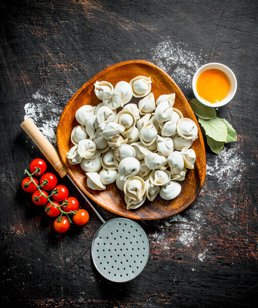 Сырая клецка на тарелке с яичным желтком и помидорами черри. На темном деревенском фоне
