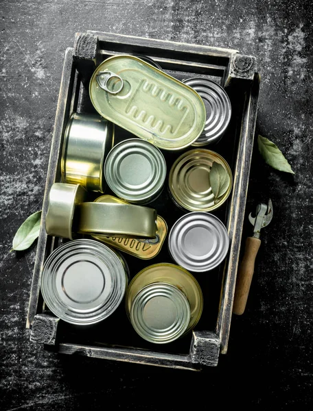 オープナー付きの箱の中の様々な閉じた缶 暗い素朴な背景に — ストック写真