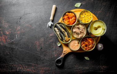 Yuvarlak kesme tahtasında konserve yiyecek. Koyu rustik arka plan üzerinde