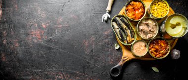 Yuvarlak kesme tahtasında konserve yiyecek. Koyu rustik arka plan üzerinde