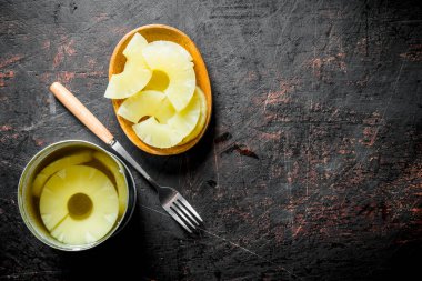 Konserve ananas bir konserve bir konserve ve bir tabak ta. Koyu rustik arka plan üzerinde