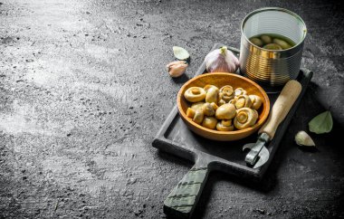 Sarımsak karanfil ve Defne yaprağı ile kesme Tahtası üzerinde Konserve mantar. Siyah rustik arka plan üzerinde