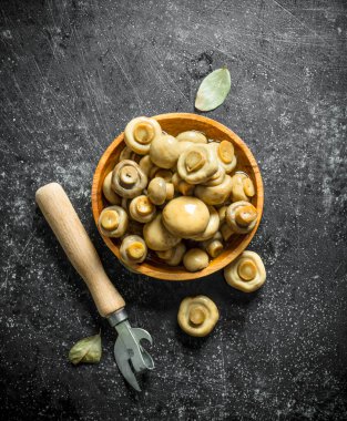 Bir açacağı ile ahşap bir tabak üzerinde konserve mantar. Koyu rustik arka plan üzerinde