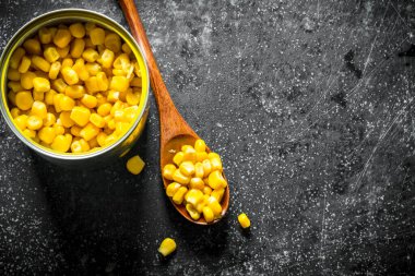 Konserve teneke ve konserve mısır ile kaşık. Koyu rustik arka plan üzerinde