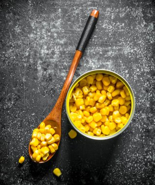 Konserve teneke ve konserve mısır ile kaşık. Koyu rustik arka plan üzerinde