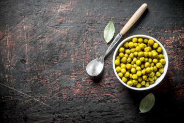 Kaşık ve Defne yaprağı ile kase de Konserve yeşil bezelye. Koyu rustik arka plan üzerinde