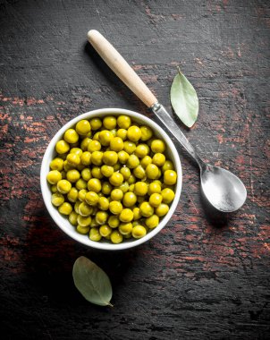 Kaşık ve Defne yaprağı ile kase de Konserve yeşil bezelye. Koyu rustik arka plan üzerinde