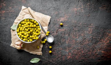 Kağıt üzerinde bir kase de konserve yeşil bezelye. Koyu rustik arka plan üzerinde