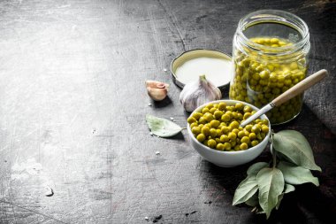 Bir kase ve Defne yaprağı ile cam bir kavanoz konserve yeşil bezelye. Koyu rustik arka plan üzerinde