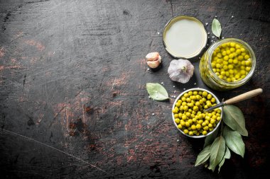 Bir kase ve Defne yaprağı ile cam bir kavanoz konserve yeşil bezelye. Koyu rustik arka plan üzerinde